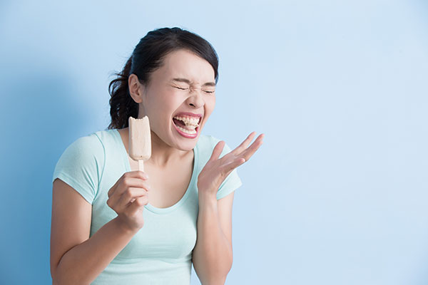 Young woman dealing with tooth sensitivity after biting into an ice cream bar.