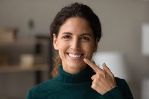 Smiling woman pointing to her teeth, showcasing a confident smile, representing the benefits of Invisalign treatment for crowded teeth in Oak Harbor.